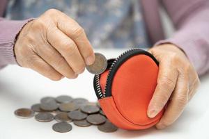asiatisk senior eller äldre gammal lady kvinna innehav räkning mynt pengar i handväska. fattigdom, sparande problem i pensionering. foto