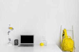 snygg vit arbetsplats med gula färger med ryggsäck och bärbar dator