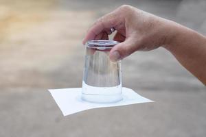 närbild hand håll och sväng en glas av vatten över ner. täckt de glas med papper. begrepp, vetenskap experimentera handla om luft och flytande tryck. lätt vetenskap ämne aktivitet, utbildning. foto