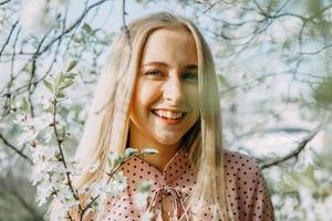 blond flicka på en vår promenad i de trädgård med körsbär blommar. kvinna porträtt, närbild. en flicka i en rosa polka punkt klänning. foto