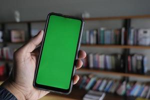 innehav smart telefon med vit skärm mot bibliotek bakgrund foto