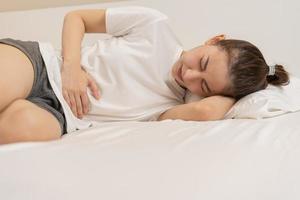 flatulens ulcus, asiatisk ung kvinna, flicka händer i mage, magont från mat förgiftning, abdominal smärta och matsmältnings problem, gastrit eller diarre. buk inflammation, menstruations- period människor. foto