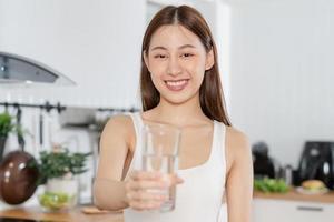 Lycklig skön, asiatisk ung kvinna, flicka dricka, smutta färsk glas av vatten för hydrat, innehav transparent glas i henne hand, törstig på Hem. hälsa vård, friska livsstil begrepp. foto