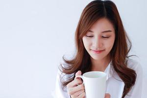 porträtt av ung asiatisk kvinna som håller en kaffekopp på en vit bakgrund.
