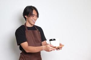 porträtt av attraktiv asiatisk Barista man i brun förkläde innehav två ta bort papper kaffe koppar. isolerat bild på vit bakgrund foto