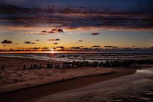 färgrik solnedgång över de putsa baltic hav med mörk himmel moln och vågbrytare foto