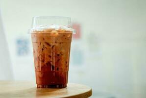 thai te, iced mjölk te med mjölk i plast kopp på trä- tabell i kaffe affär. foto