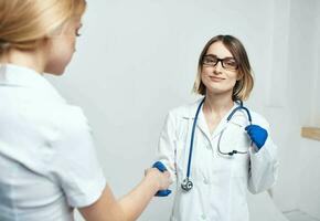 de sjuksköterska skakningar händer med de patient på en ljus bakgrund och blå handskar med en stetoskop foto