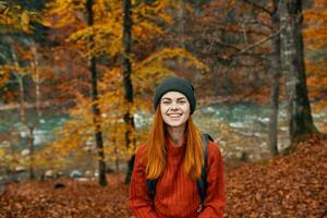 glad kvinna resor i de höst skog i natur nära de flod och lång träd i de bakgrund foto