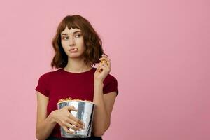 upphetsad förvirrad söt rödhårig lady i röd t-shirt med popcorn redo för film kväll Framställ isolerat på över rosa studio bakgrund. kopia Plats baner. mode bio begrepp. underhållning erbjudande foto