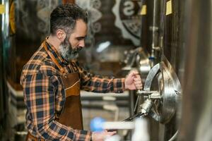 man är arbetssätt på hantverk öl fabrik. han är rörelse maskineri i bryggeri. små familj företag, produktion av hantverk öl. foto