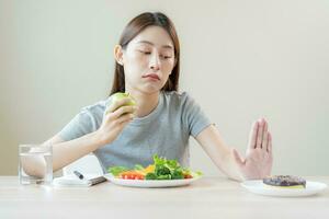 diet, bantning asiatisk ung kvinna eller flicka använda sig av hand skjuta på ut, förneka ljuv munk och välja grön sallad grönsaker, äta mat för Bra friska, hälsa när hungrig. stänga upp kvinna vikt förlust person. foto