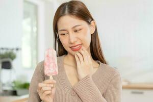 hälsa asiatisk ung kvinna rörande kind, uttryck, lidande från tandvärk, förfall eller känslighet hålighet molar- tand, tänder eller inflammation äta kall is grädde på Hem. känslig tänder människor. foto