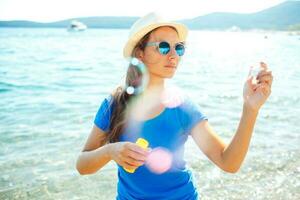 glad ung flicka som blåser såpbubblor på stranden foto
