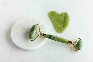 grön jade vält och gua sha sten massager för ansikte på vit marmor. foto