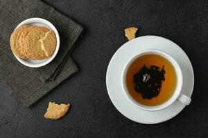kopp av te med småkakor på svart bakgrund. foto