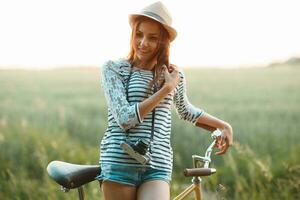 härlig ung kvinna står i en fält med henne cykel foto