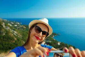 flicka i de hatt framställning selfie förbi de smartphone på de bakgrund av hav kust, adriatisk hav foto