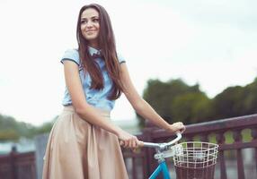 ung skön, elegant klädd kvinna med cykel i de parkera eller utomhus- foto