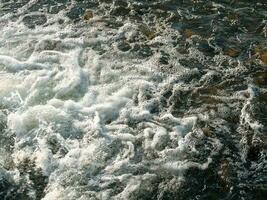 strömmande mörk vatten textur. vit vatten skum, små bubbelpool, vatten bakgrund. foto