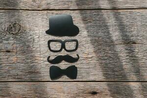 Lycklig fäder dag klistermärke, hatt, glasögon, svart mustasch på en trä- bakgrund. hipster objekt. fars dag är en Semester foto