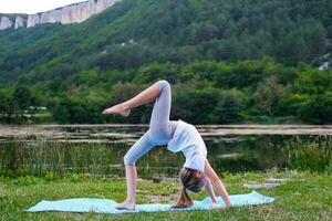 en liten flicka gör en bro, böjning henne tillbaka i natur. en flexibel barn, håller på med gymnastik övningar. sporter, inlärning, kondition, stretching, yoga, aktiva livsstil begrepp foto