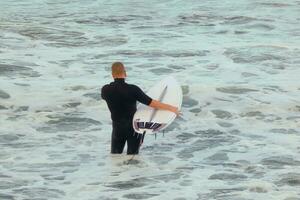 surfare få redo till stiga på de vatten och gående med de styrelse längs de Strand. foto