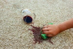 glas av röd vin föll på matta, vin spillts på matta. kvinna hand rengör de matta med en svamp och rengöringsmedel. foto