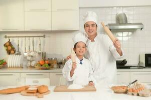 ung asiatisk far och hans son bär kock enhetlig bakning tillsammans i kök på Hem foto
