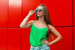 skön Lycklig flicka i en eleganta solglasögon nära en modern röd vägg foto