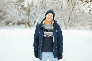 Lycklig ung man i vinter- kläder och eleganta modern stickat Tröja gående i en vinter- parkera. foto