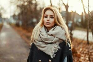 skön ung blond flicka i täcka och scarf på de bakgrund av höst parkera. foto