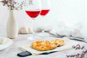 två hjärta formad pizzor på papper och två glasögon av vin på en uppsättning tabell för hjärtans dag firande foto