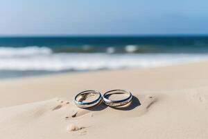 två bröllop ringar i de sand på de bakgrund av en strand och hav. ai genererad foto