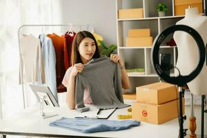 mode bloggare begrepp, ung asiatisk kvinnor försäljning kläder på video streaming.startup små företag sme, använder sig av smartphone eller läsplatta tar motta och kontroll foto