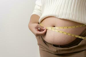 ett fetma använder sig av mätning tejp till visa de verklig storlek. knubbig fett kvinna använder sig av mäta tejp på mage. foto
