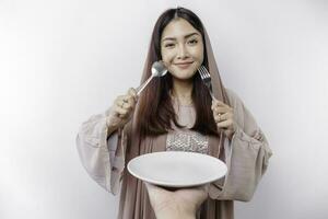 en leende asiatisk muslim kvinna är fasta och hungrig och innehav och pekande till en tallrik foto