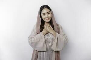 Lycklig uppmärksam tacksam ung asiatisk muslim kvinna med henne hand på henne bröst leende isolerat på vit bakgrund foto