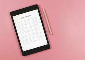 platt lägga av digital läsplatta med mall 30 dag utmaning på skärm, rosa nål penna, isolerat på rosa bakgrund. foto