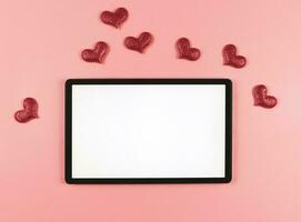 platt lägga av digital läsplatta med tom vit skärm, röd glitter hjärtan isolerat på rosa bakgrund. foto