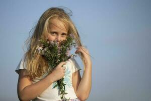 skön liten flicka med en bukett av vild blommor mot de himmel. foto