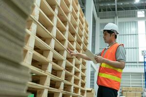 asiatisk manlig fabrik inspektera lastpall i lager eller lager och kolla upp stock produkt. transport logistisk företag frakt, leverans till kunder. inspektion, magasin, lagring, fabrik foto