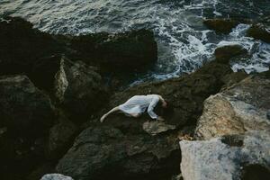 skön ung kvinna i lång vit klänning våt hår liggande på en klippig klippa sommar semester begrepp foto