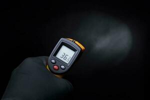 en handskar hand innehar ett industriell termometer på en svart bakgrund. foto