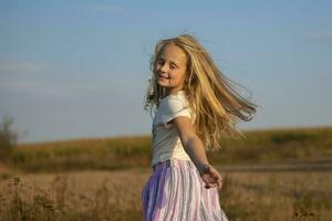 skön liten flicka med en bukett av vild blommor på en bakgrund av de himmel. en Lycklig barn på en sommar äng. foto