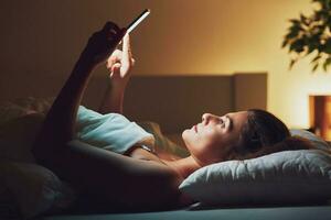 kvinna på natt i säng med telefon foto