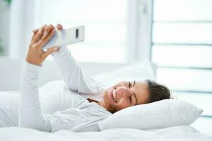 ung brunett kvinna med smartphone på de säng foto