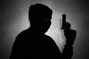 mystisk man bär svart luvtröja innehav en pistol, skytte med en pistol. silhuett och mörk begrepp bild foto