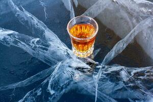på de knäckt is av de sjö är en glas av whisky. kyld whisky. blå is med skön djup vit sprickor. topp se från de sida. reklam alkohol Produkter. horisontell. foto