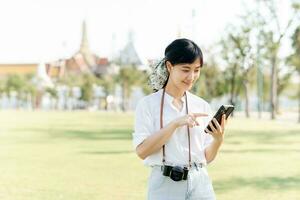 porträtt skön ung asiatisk kvinna med smartphone på sommar Semester semester resa med de stor palats i en bakgrund på Bangkok, thailand foto